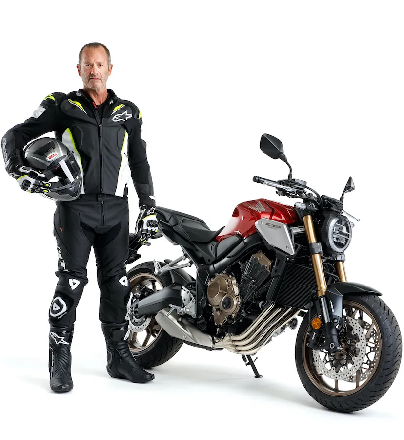Man standing next to a motorcycle while holding a helmet on his arm