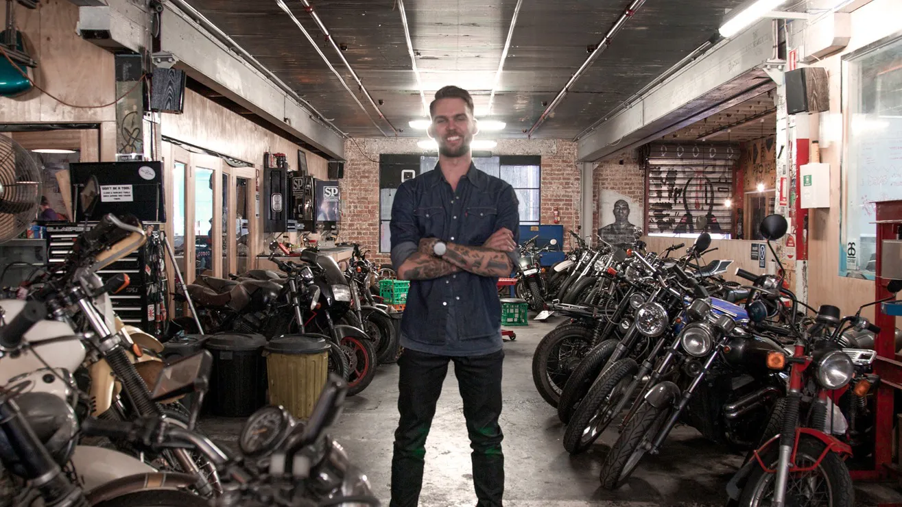Jimmy Goode standing on a large room, surrounded by motorcycles